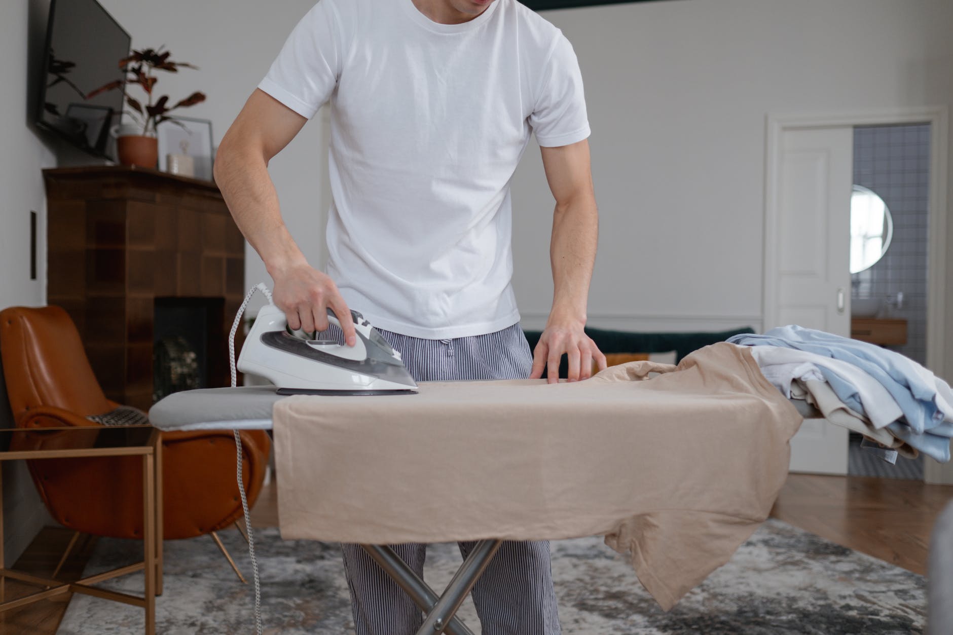 man in white crew neck shirt ironing brown shirt