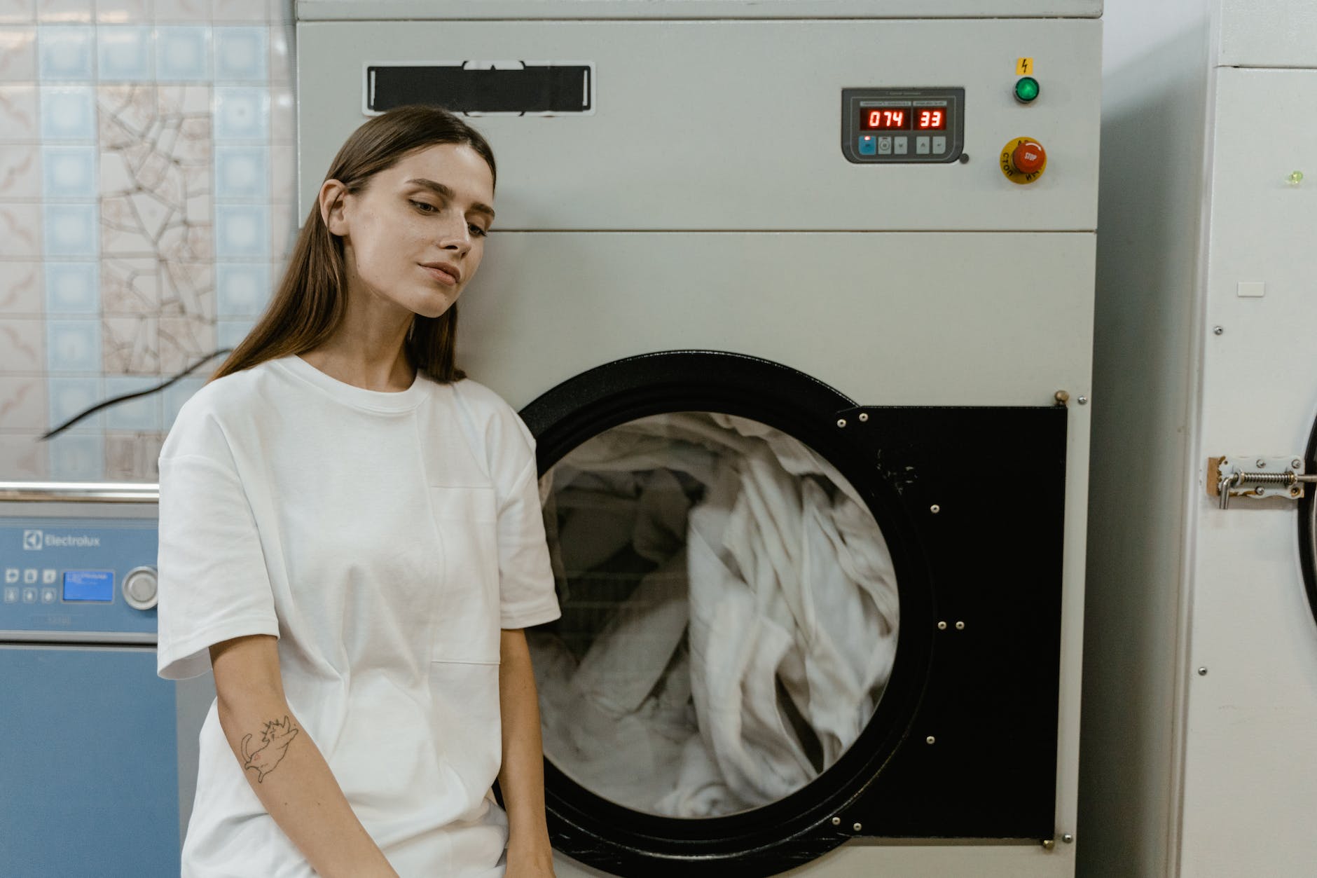 woman in white shirt sitting beside white and black washing machine