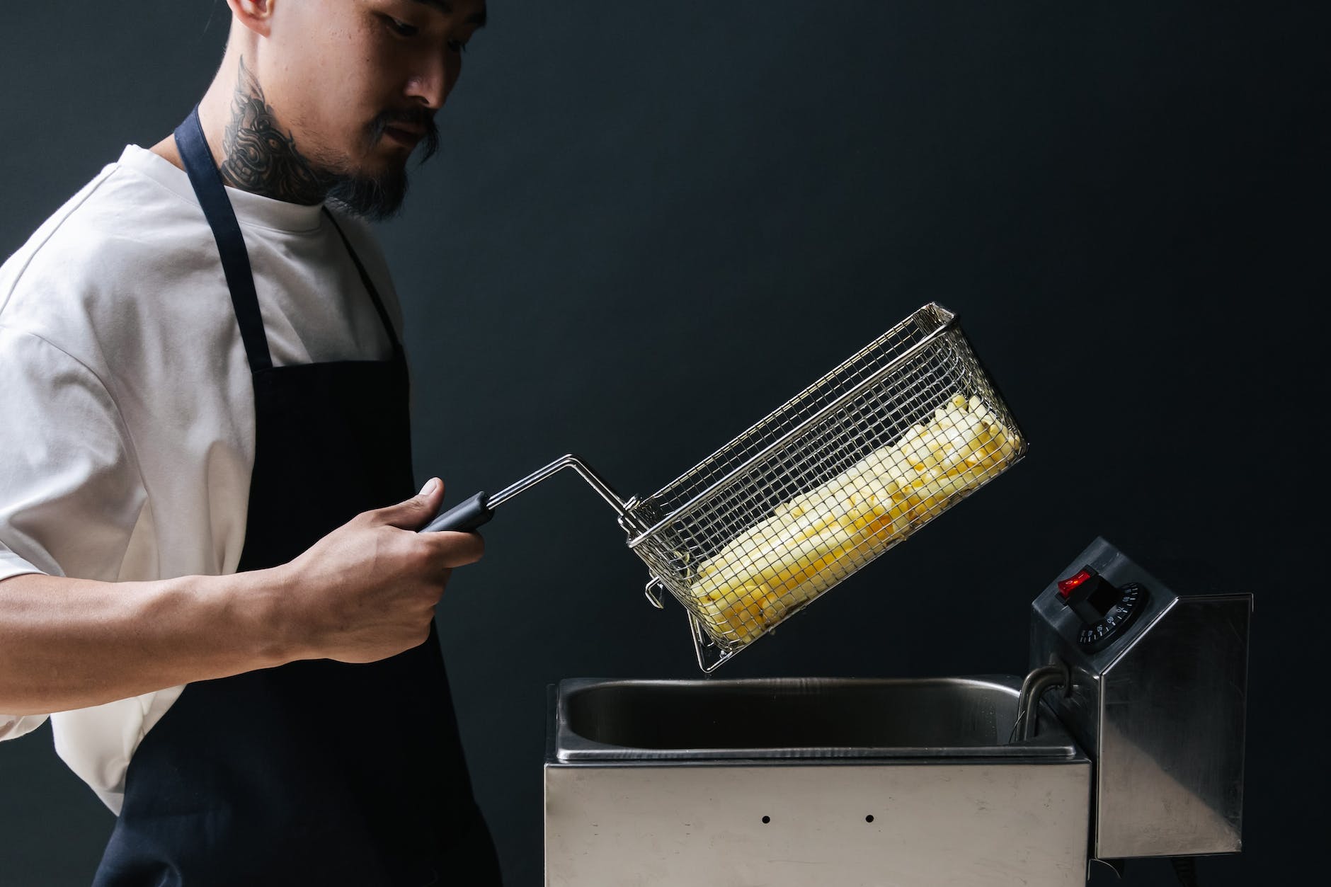 a man with black apron holding a stainless basket over a stainless deep fryer